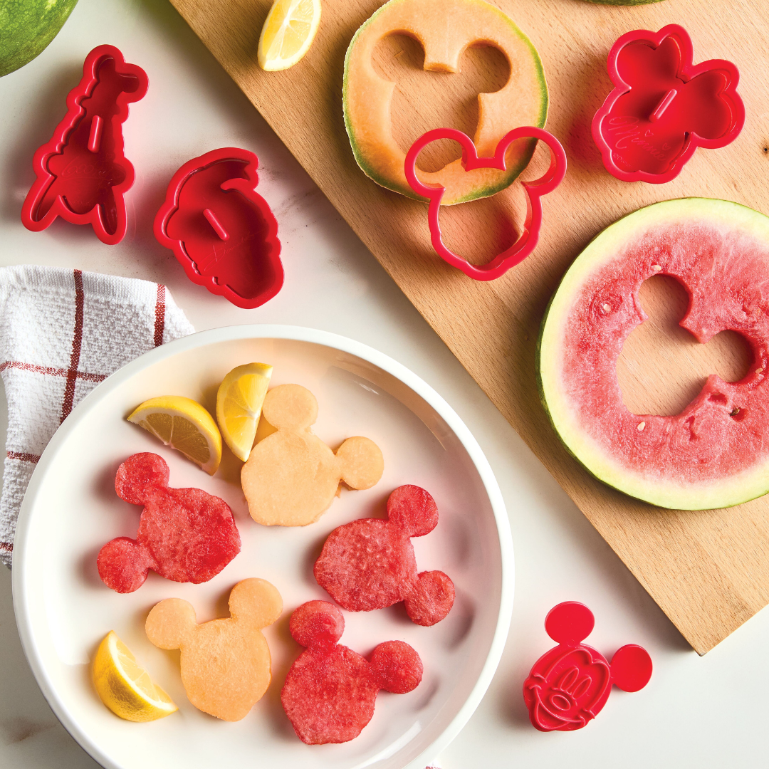 Fruit slices cut into cartoon shapes using the Bake with Mickey Mouse 8-Piece Cookie Cutter and Stamp Set, featuring Mickey and Friends, arranged on a board and plate.
