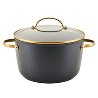 The Forged Induction Ceramic 6-Quart Stockpot With Lid is crafted from forged aluminum and comes with a glass lid and gold handles. This black pot, set against a white background, boasts an induction-ready ceramic nonstick surface for effortless cooking and easy cleanup.