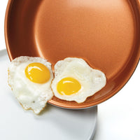 Two fried eggs being served from a copper non-stick frying pan.