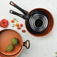 Copper pans with artichokes and tomatoes on a speckled surface.