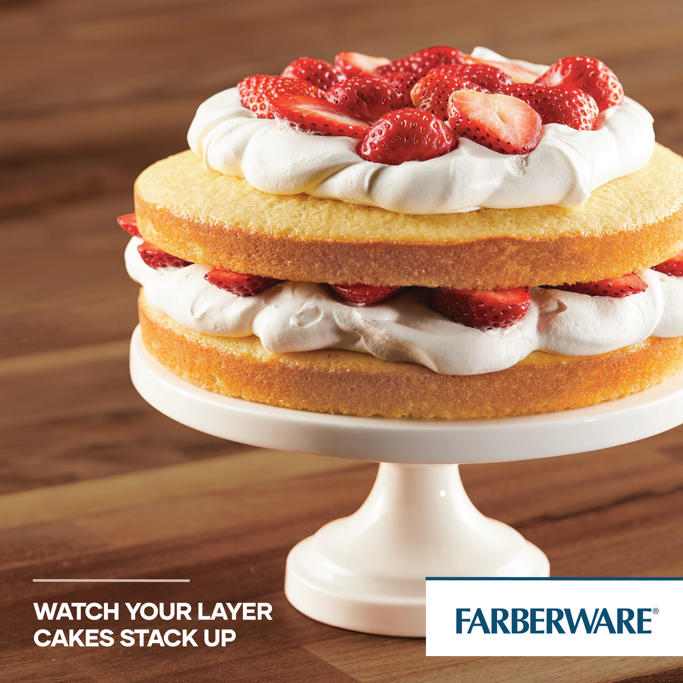 A two-layer cake adorned with whipped cream and strawberries is elegantly displayed on a cake stand, effortlessly achieved using the 2-Piece Nonstick Round Cake Pan Set for even heating.