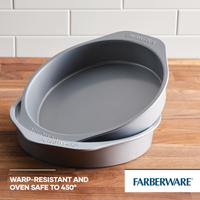 Two pans from the 2-Piece Nonstick Round Cake Pan Set, designed with heavy-gauge steel for durability, are stacked on a wooden surface. These gray baking essentials ensure even heating for all your baking needs.