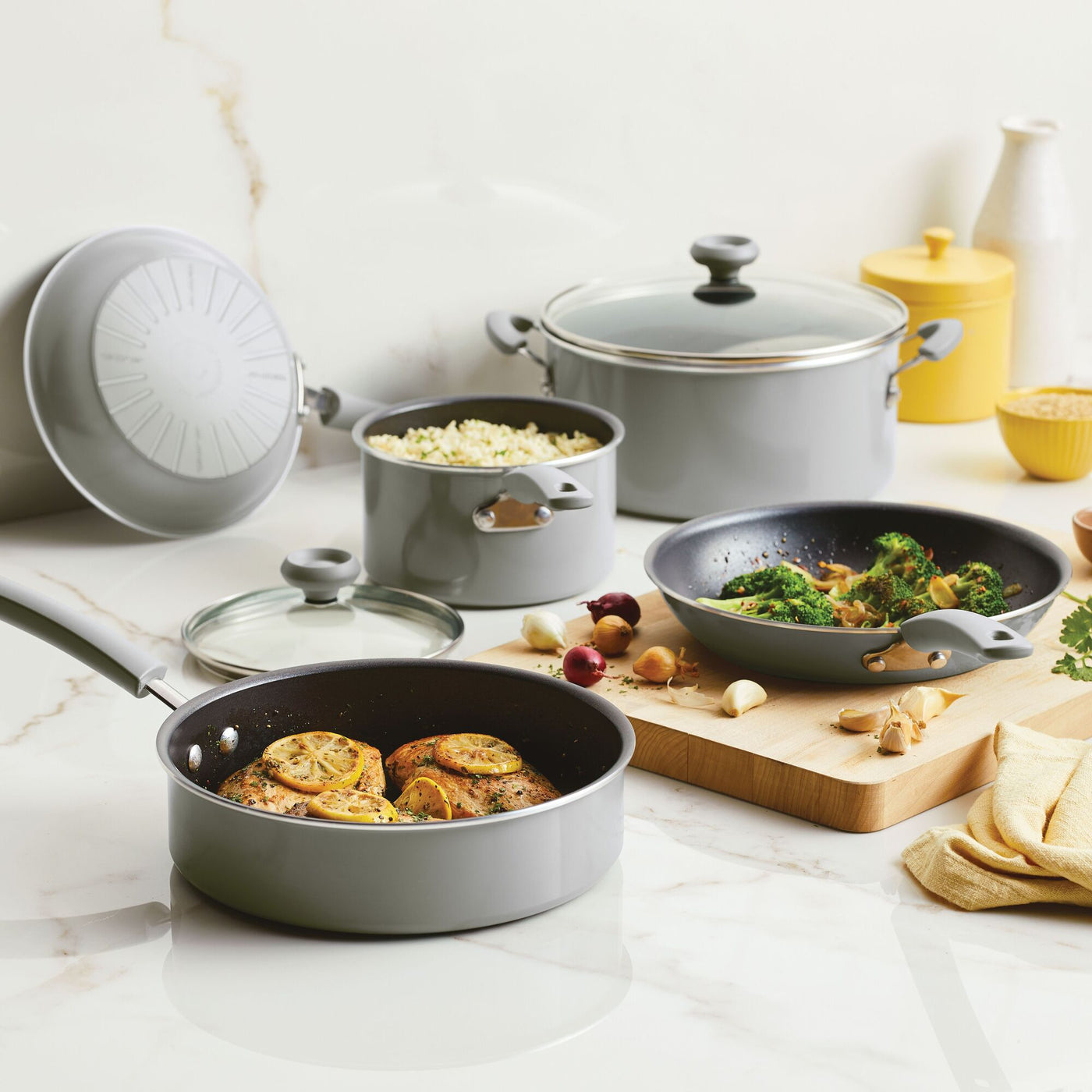 A 12-piece nonstick cookware set rests elegantly on a marble countertop, filled with delicious food.