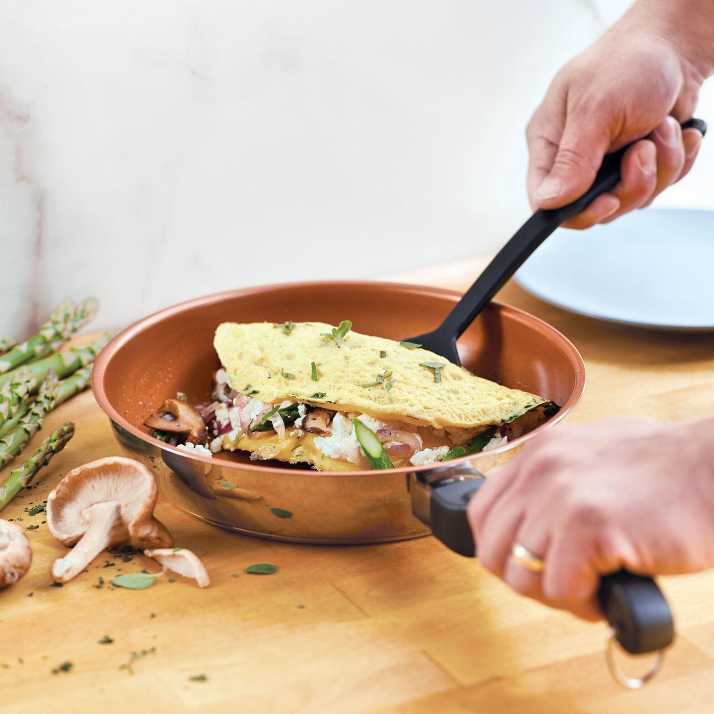 With the Classic Traditions Ceramic Stainless Steel cookware, the person skillfully folds an omelette filled with mushrooms and asparagus, epitomizing kitchen essentials for any culinary enthusiast.