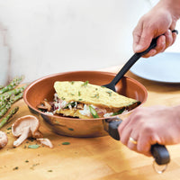 With the Classic Traditions Ceramic Stainless Steel cookware, the person skillfully folds an omelette filled with mushrooms and asparagus, epitomizing kitchen essentials for any culinary enthusiast.