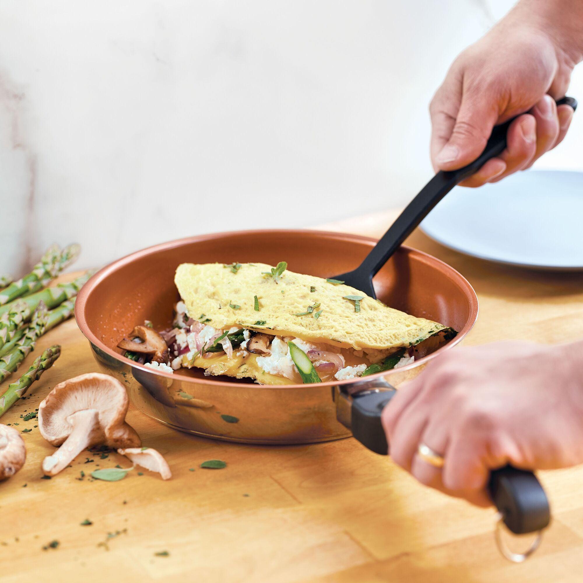 With the Classic Traditions Ceramic Stainless Steel cookware, the person skillfully folds an omelette filled with mushrooms and asparagus, epitomizing kitchen essentials for any culinary enthusiast.