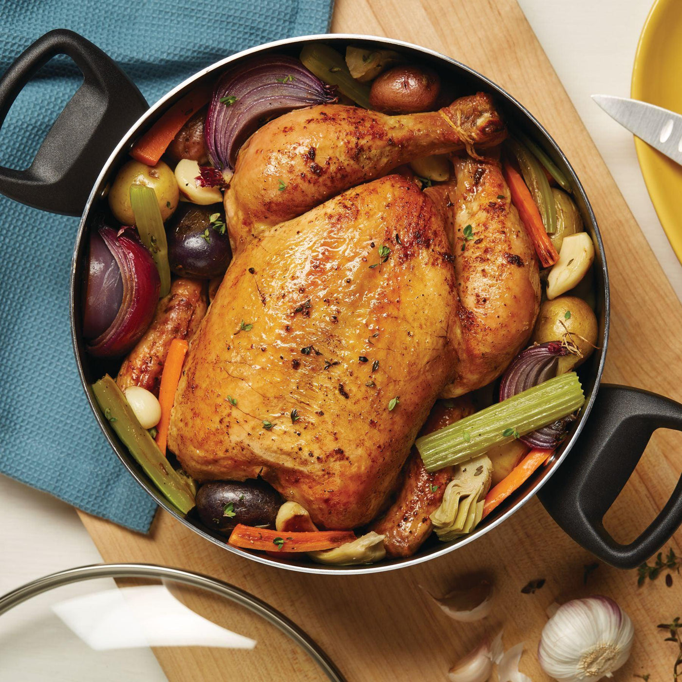 A 10.5-Quart Nonstick Stockpot filled with roasted chicken and vegetables rests on a cutting board, ideal for serving family-sized portions and ensuring easy cleanup thanks to its dishwasher-safe design.