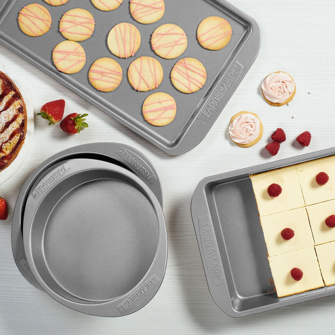 Baked goods, fresh cookies, and strawberries grace the countertop alongside cookie pans with a beautifully decorated cake.