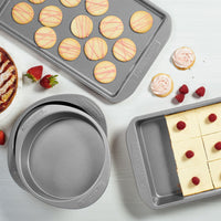 Baked goods, fresh cookies, and strawberries grace the countertop alongside cookie pans with a beautifully decorated cake.