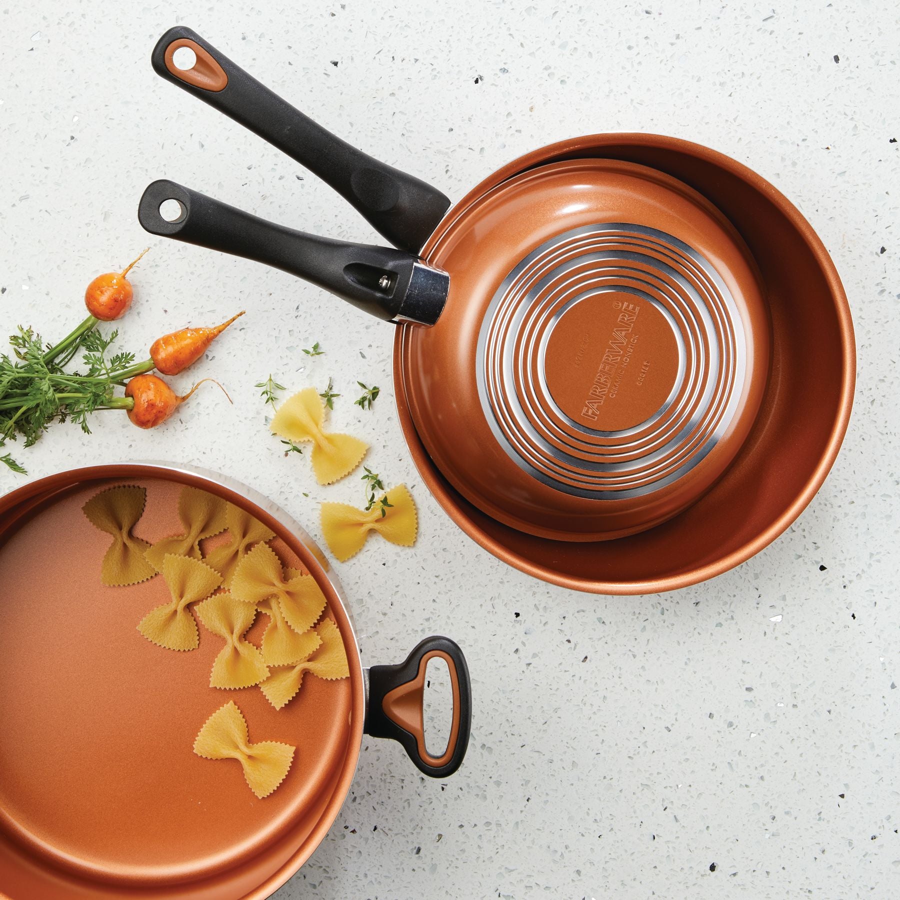 The 12-Piece Copper Ceramic Nonstick Cookware Set, which includes pans with advanced CopperSlide technology, pairs beautifully with bowtie pasta on a speckled countertop, blending aesthetics and functionality perfectly.