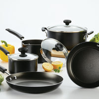 The Nonstick Frying Pan, a stylish piece with durable aluminum construction in black, is elegantly displayed next to fresh vegetables and halved lemons on an immaculate white surface.