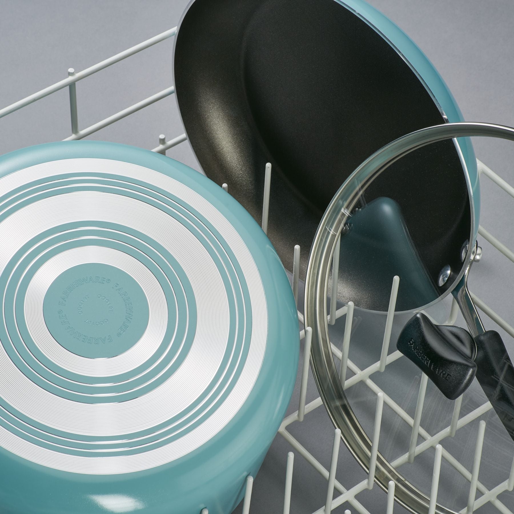 The 15-Piece Nonstick Cookware Set, featuring DiamondMax technology, sits elegantly in a dish rack on a gray surface with its teal pans and lid.