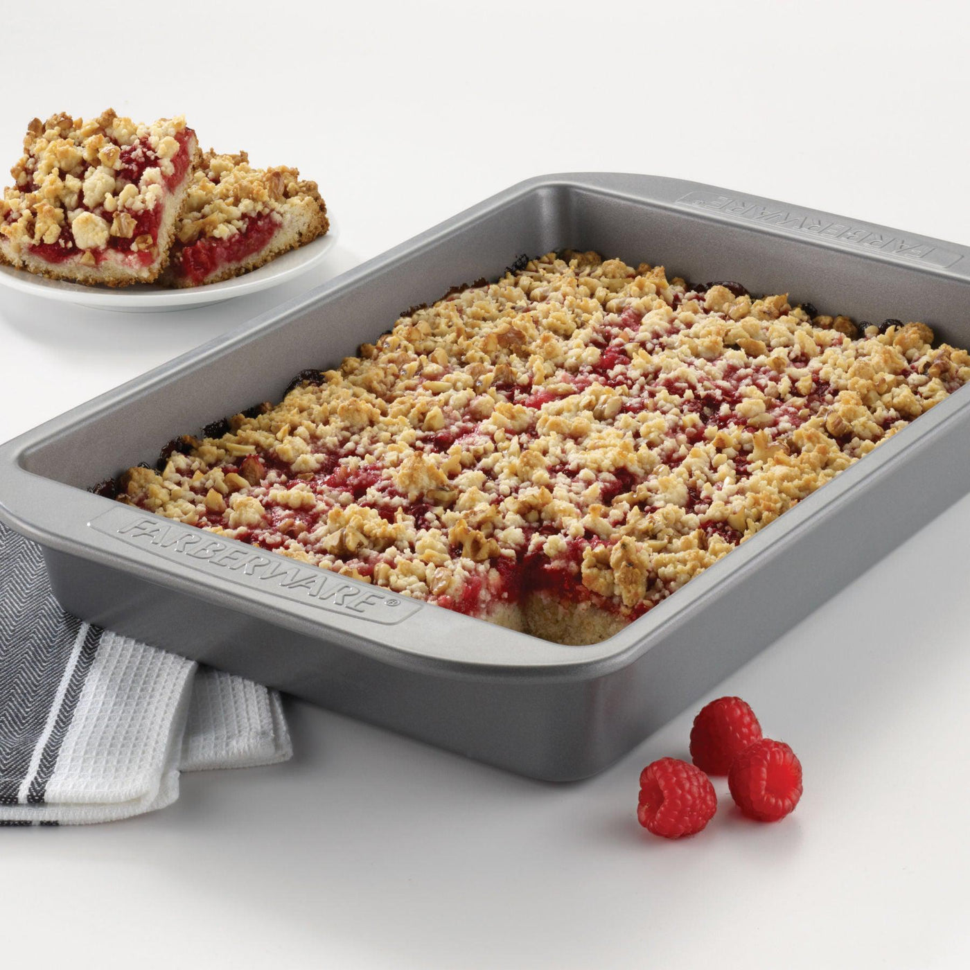 Baked raspberry crumble in an even-heating 9" x 13" Rectangular Cake Pan, with a slice on a plate nearby.
