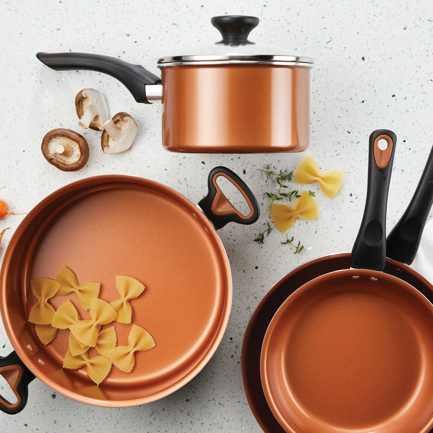 The 12-Piece Copper Ceramic Nonstick Cookware Set, equipped with advanced CopperSlide technology, is ideal for easily cooking pasta and mushrooms on a spotless white countertop.