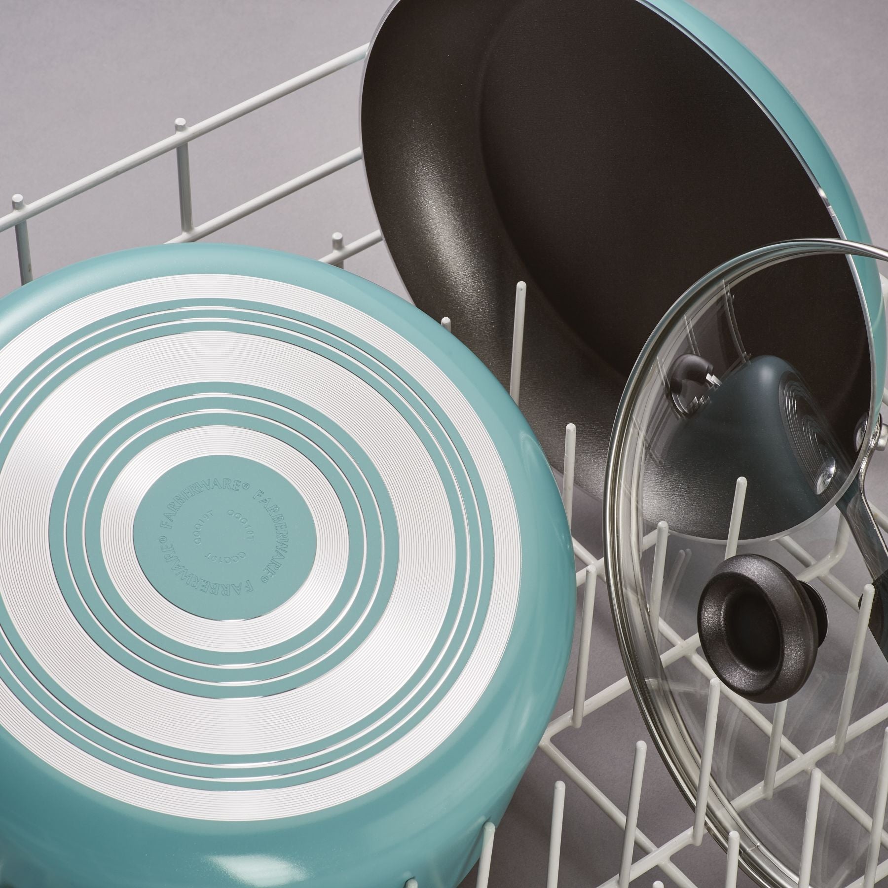 The Nonstick Frying Pan, made with durable aluminum construction, is neatly placed in the dishwasher rack alongside a pot lid.