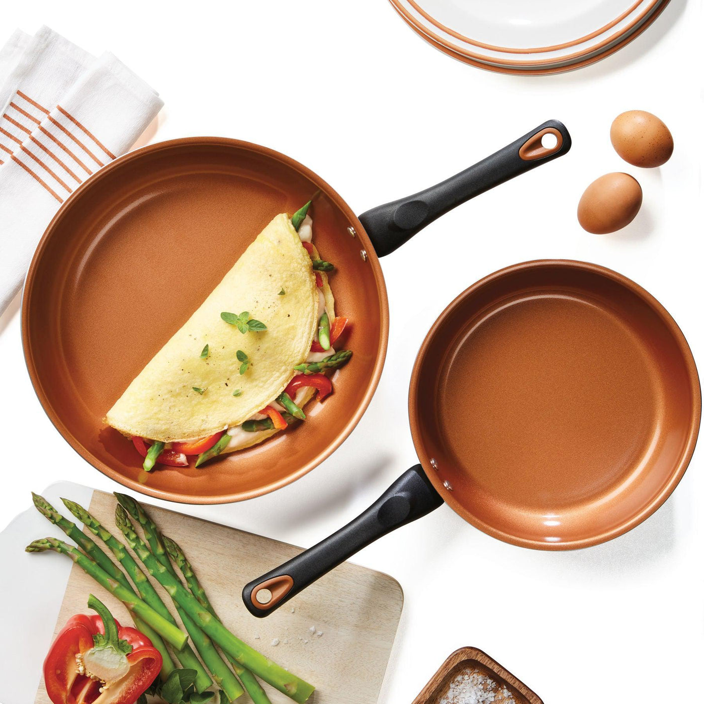 A pair of skillets from the 12-Piece Copper Ceramic Nonstick Cookware Set cradles an omelet accompanied by asparagus and eggs.
