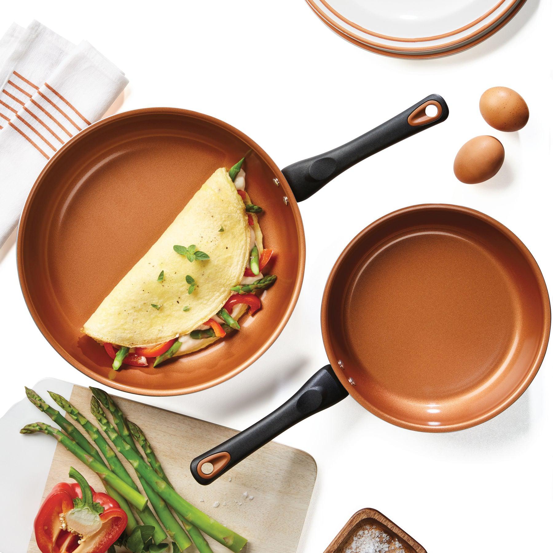 A pair of skillets from the 12-Piece Copper Ceramic Nonstick Cookware Set cradles an omelet accompanied by asparagus and eggs.