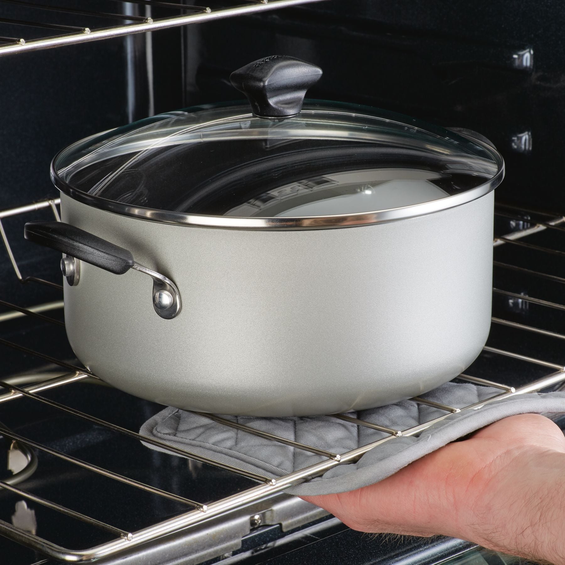 A person carefully places a pot from the 15-Piece Nonstick Cookware Set, made of heavy gauge aluminum and with a lid, in the oven using an oven mitt.