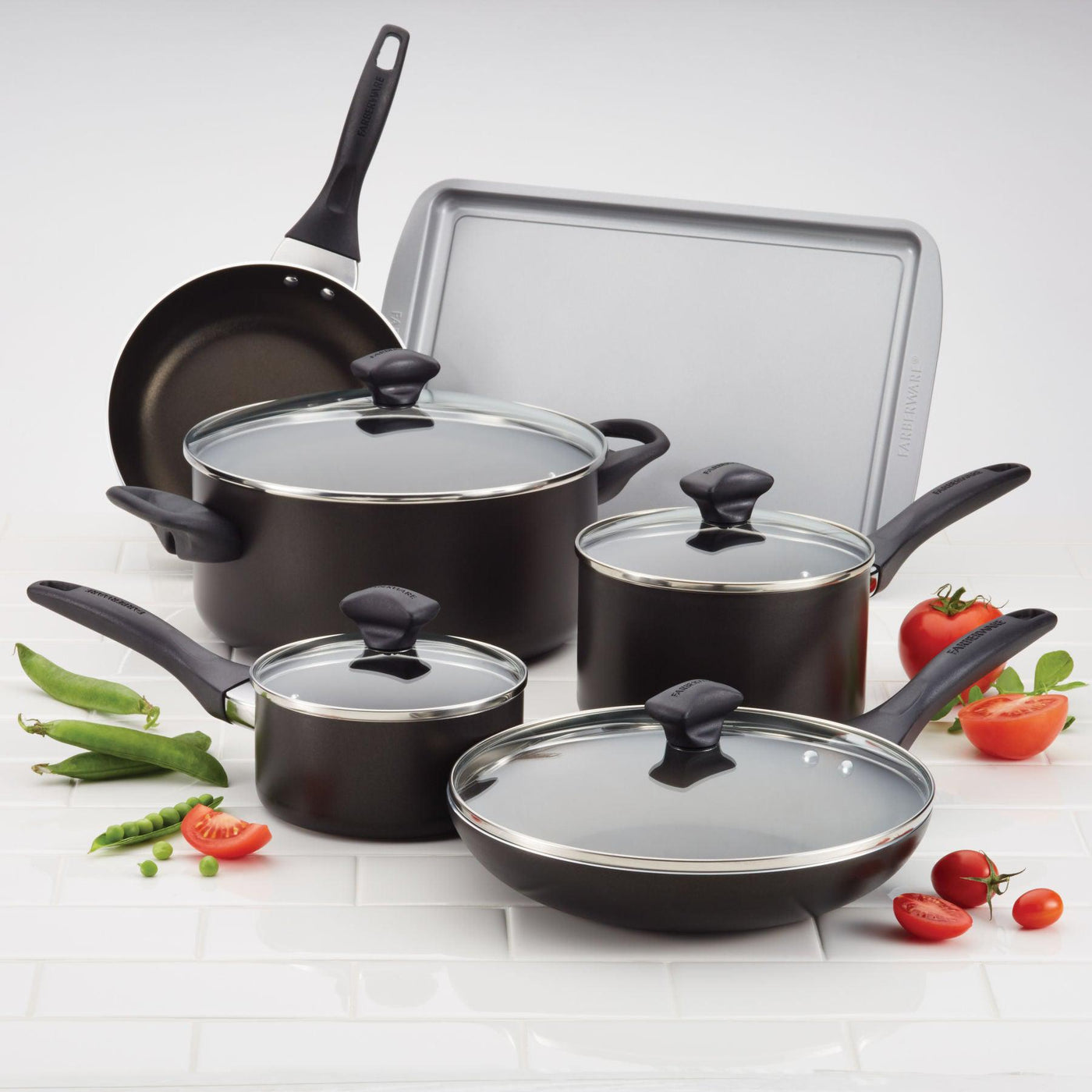 A 15-Piece Nonstick Cookware Set in black, complete with lids, rests on a white surface with tomatoes nearby.