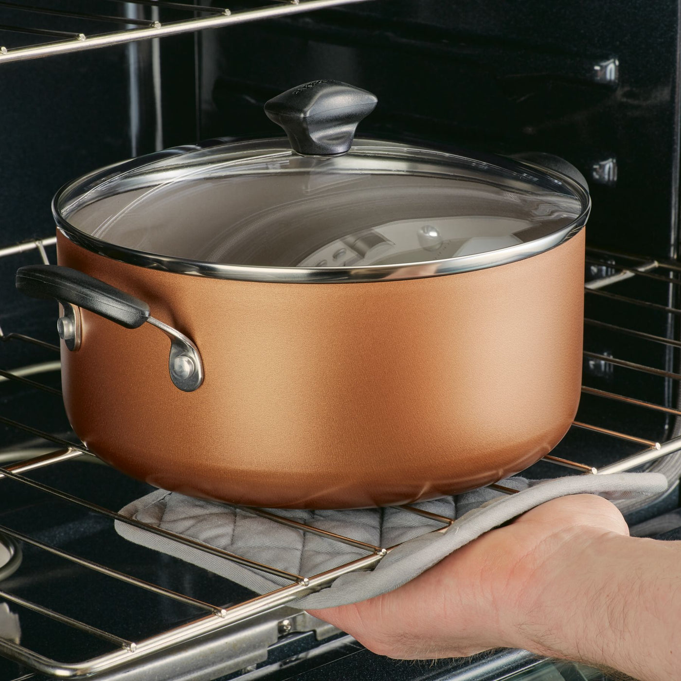 Wearing an oven mitt, a person carefully removes a pot from the 15-Piece Nonstick Cookware Set, known for its heavy gauge aluminum and DiamondMax technology, from the oven.