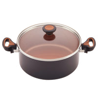 A sleek black pot from the 12-Piece Copper Ceramic Nonstick Cookware Set features CopperSlide technology, comes with a glass lid, and is enhanced by vibrant orange handle accents for an effortless cooking experience. It is also dishwasher safe for added convenience.